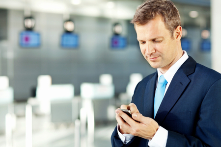 Smart corporate businessman text messaging on smart phone at an Airport. Horizontal shot.